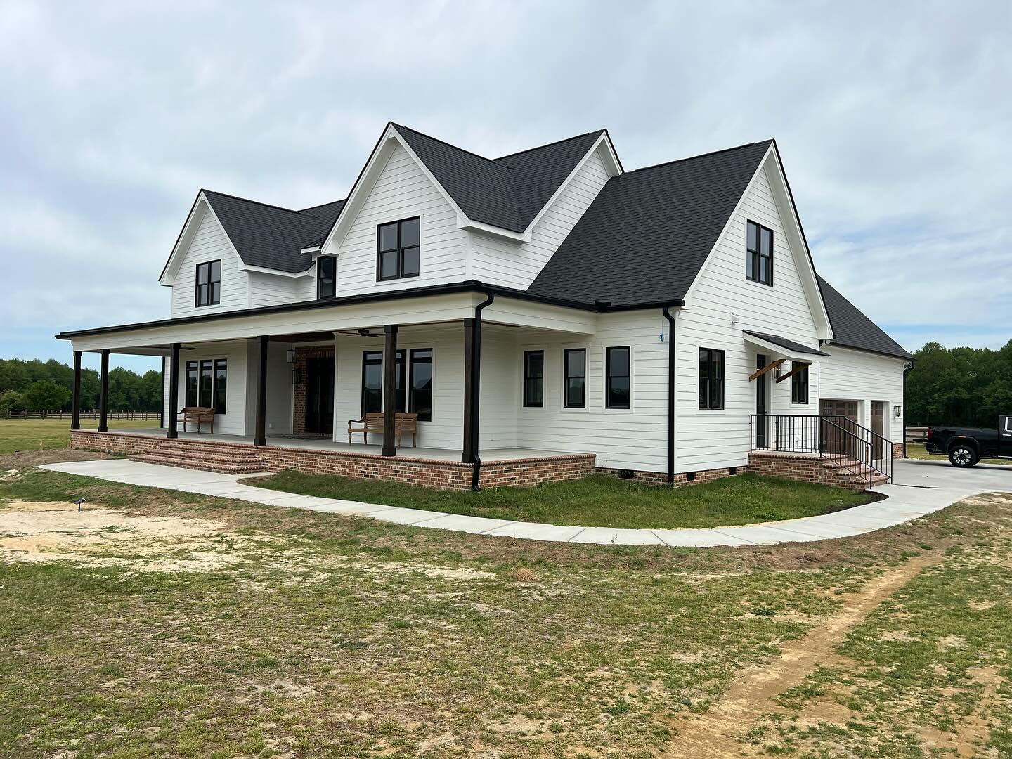 A finished custom farmhouse in Johnston County, North Carolina, with a wraparound porch, black windows and a brick foundation