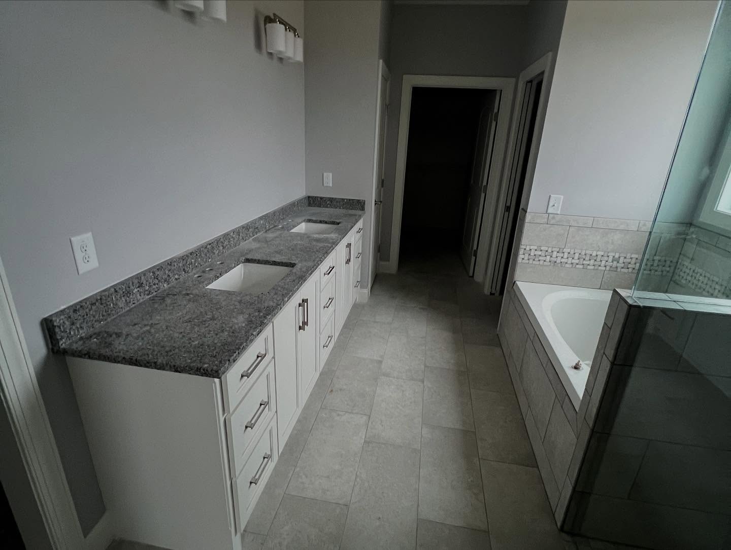 Primary bathroom with a long double vanity in white cabinetry with granite countertops, tile flooring, and a garden tub beside a glass shower