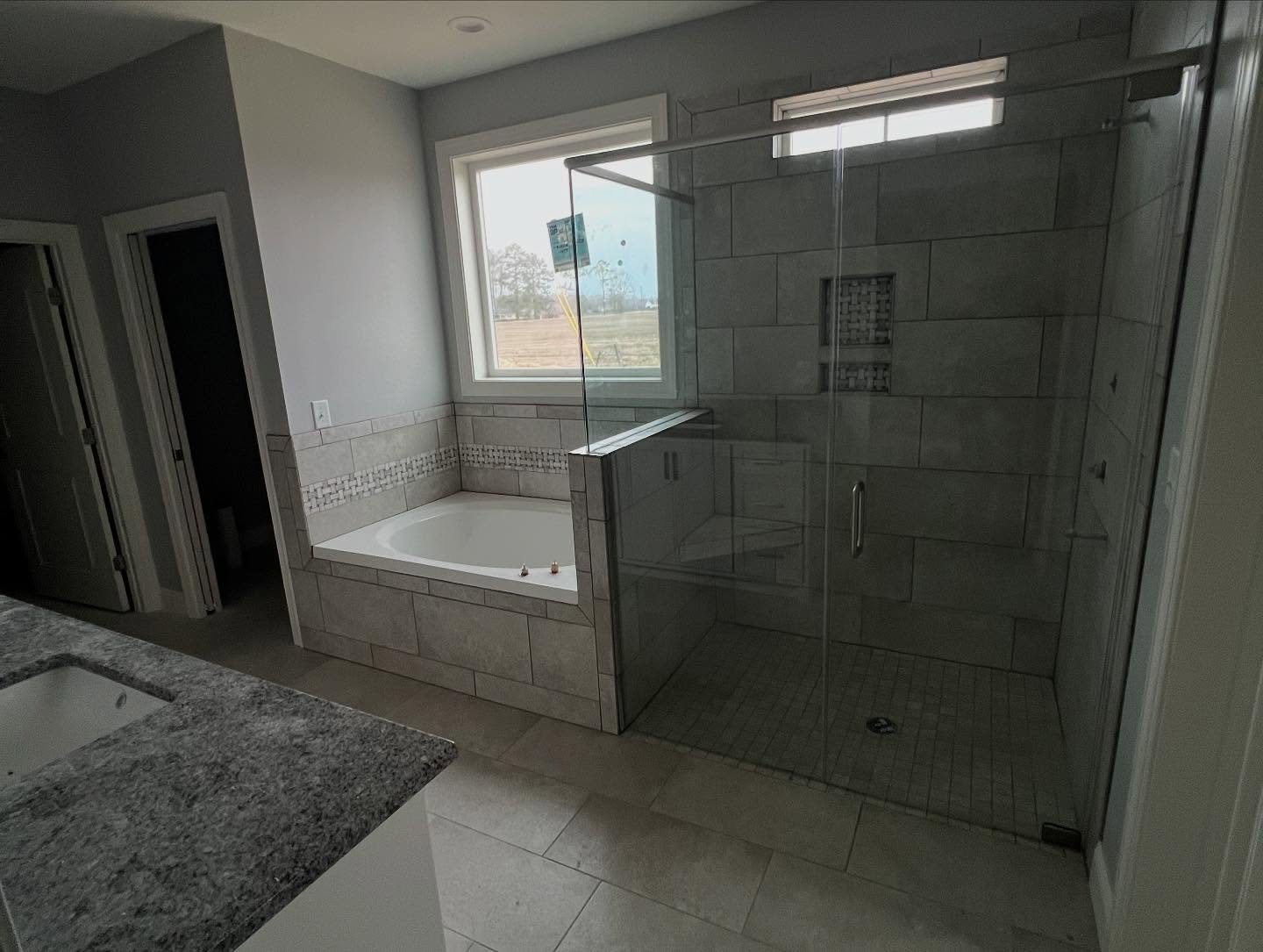 Primary bathroom with a large tiled walk-in shower behind glass doors, a tiled recessed niche, and a garden tub set into a tiled surround under a window