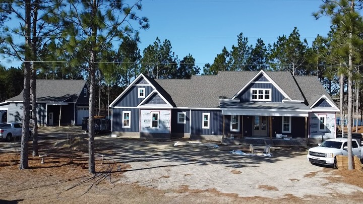 Custom home in blue board and batten siding nearing completion, set among pine trees