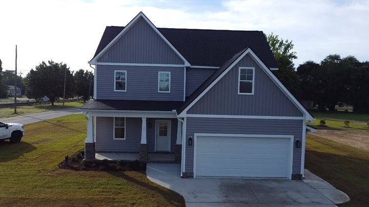 Completed two story custom home with grey siding, a covered front porch and an attached two car garage