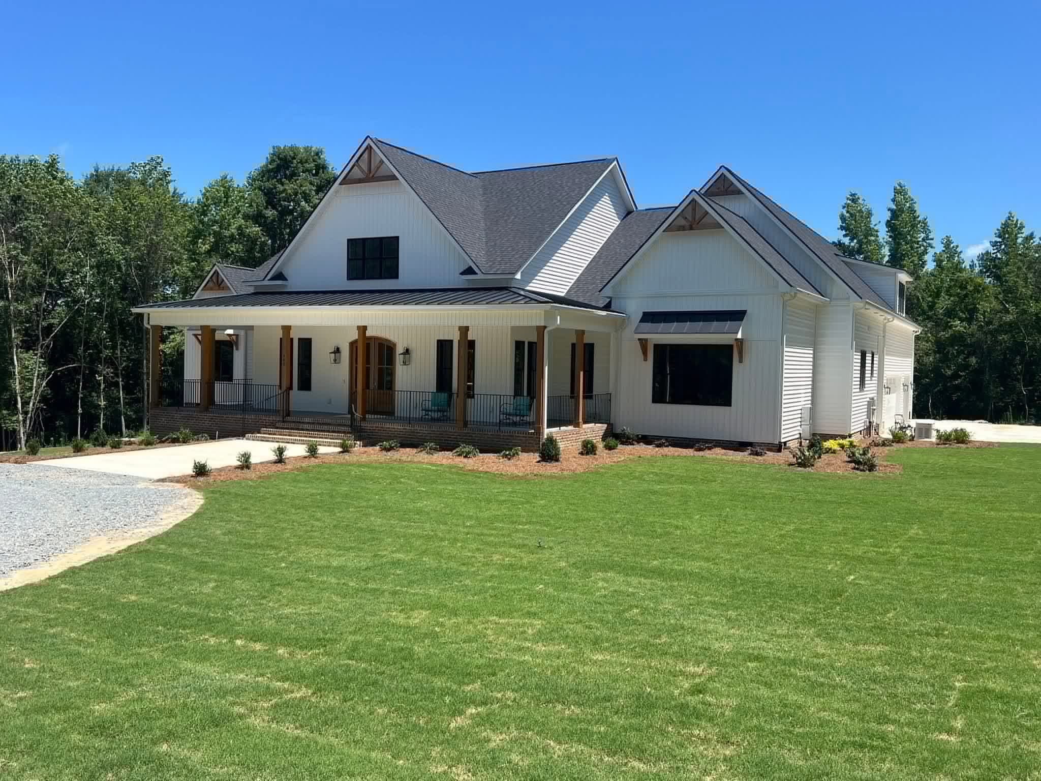 White farmhouse style custom home seen from the side, with a deep covered porch on cedar posts, gable trusses and a standing seam porch roof