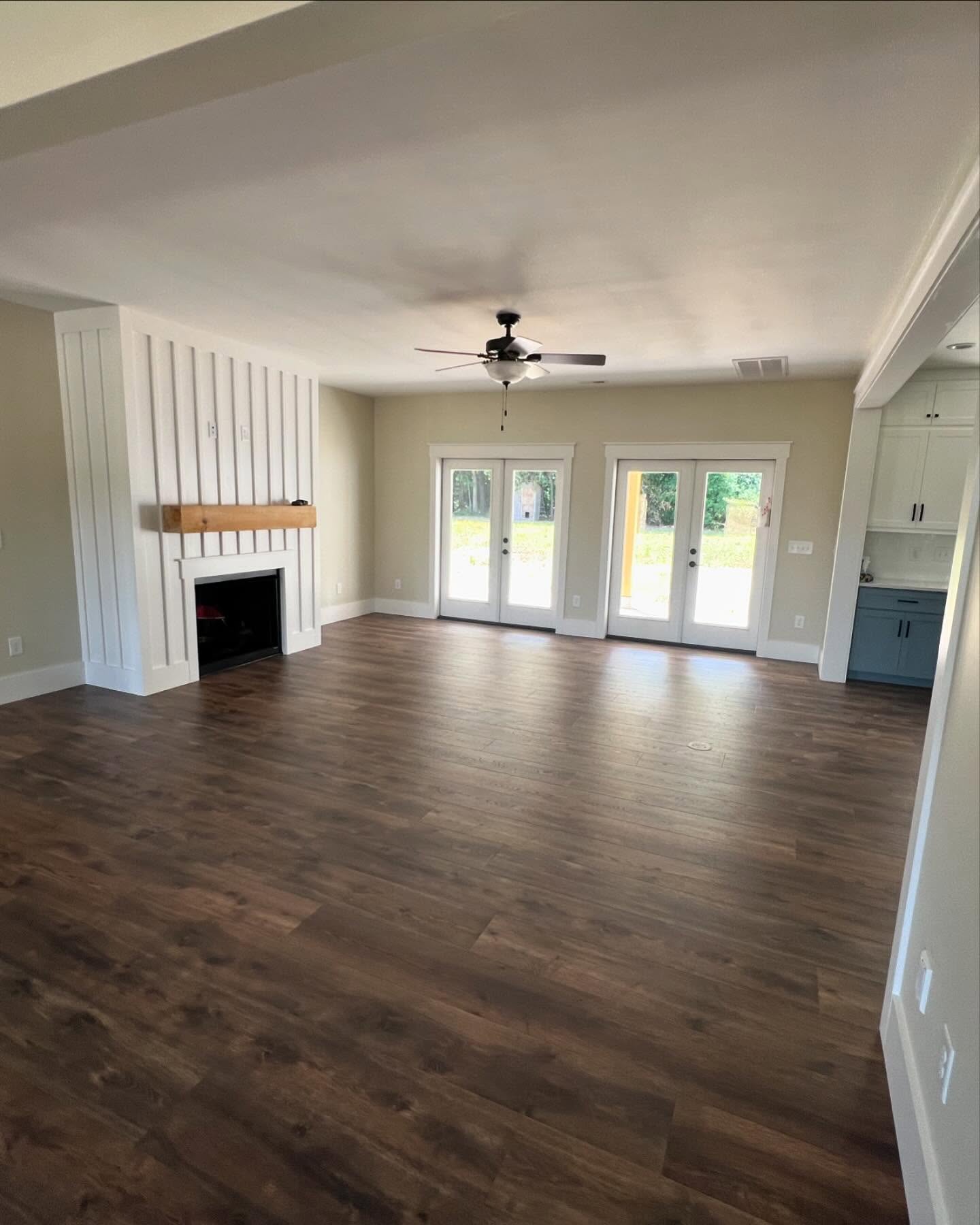 Fireplace with a floor to ceiling white board and batten surround and a rough timber mantel, in a finished living room with wide plank floors and French doors to the rear yard