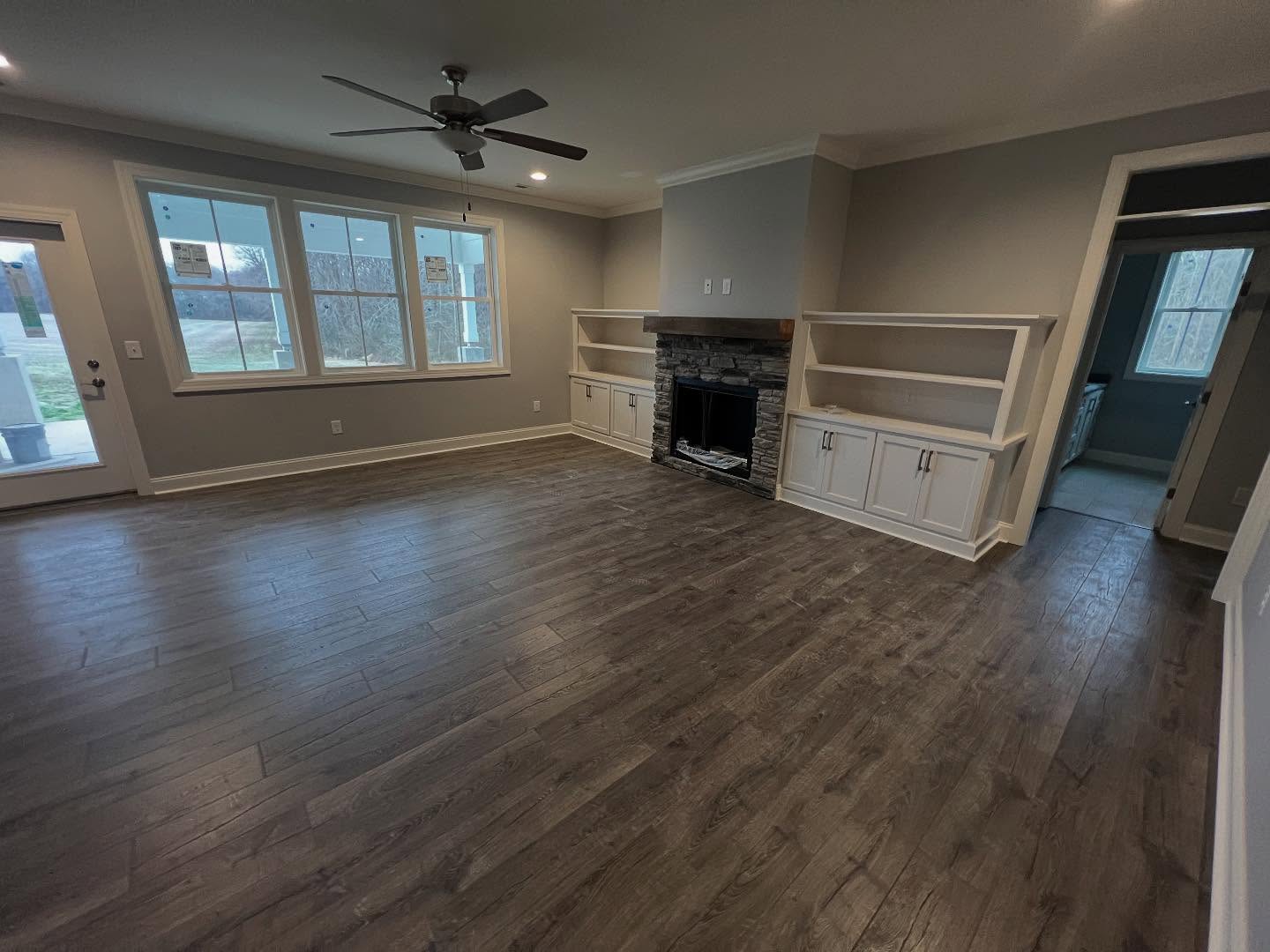 Stone fireplace with a raised hearth and rough timber mantel, flanked by built-in cabinets and open shelving in a finished great room