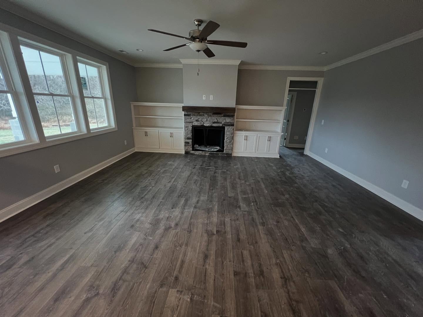 Stacked stone fireplace with a timber mantel and white painted built-in shelving and cabinets on both sides, in a finished living room with wide plank floors