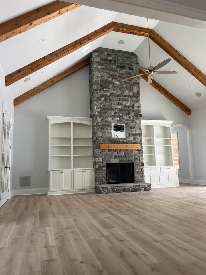 Stone fireplace running to the peak of a vaulted great room ceiling with exposed cedar beams, a timber mantel and white built-ins on both sides