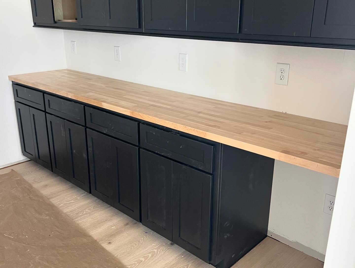 Run of black shaker cabinetry with a butcher block countertop and upper cabinets, in a pantry area of a custom home