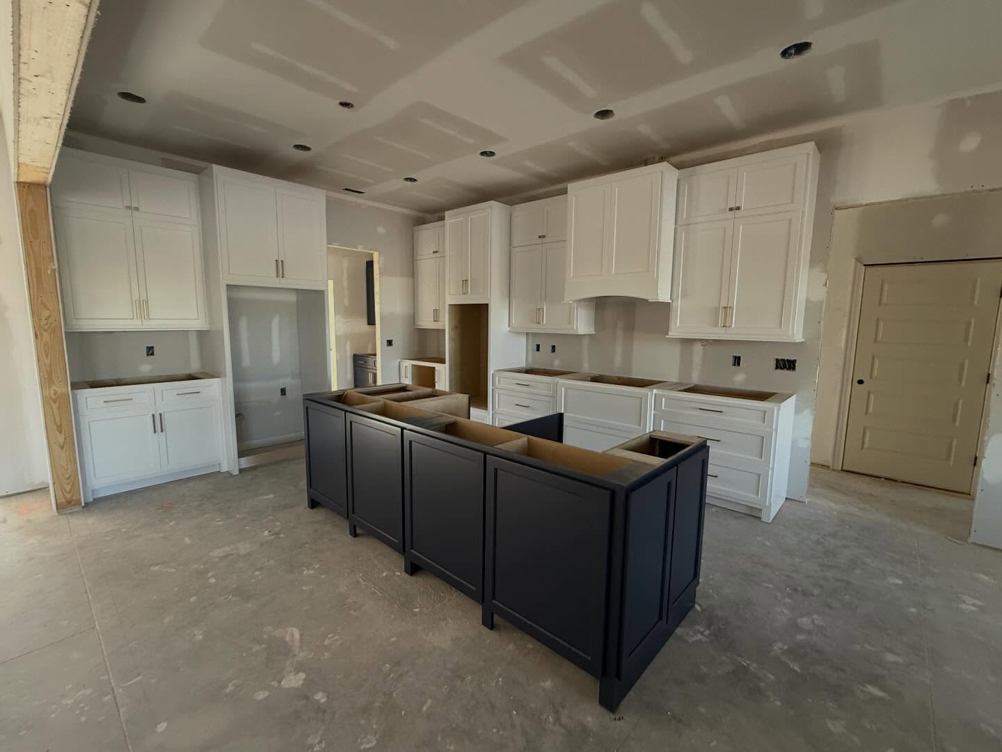 Custom kitchen with white shaker wall cabinets, a built-in vent hood surround and a navy blue island, photographed before countertops are installed