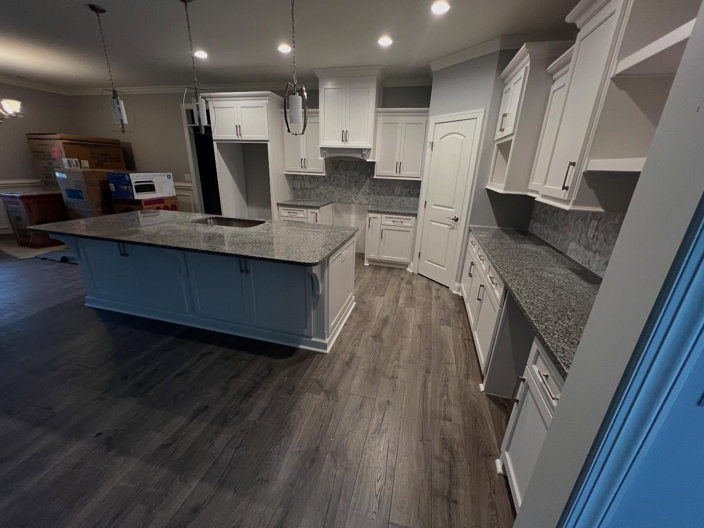 Wide view of a finished custom kitchen with a blue painted island, white perimeter cabinetry, granite countertops and a built-in vent hood surround