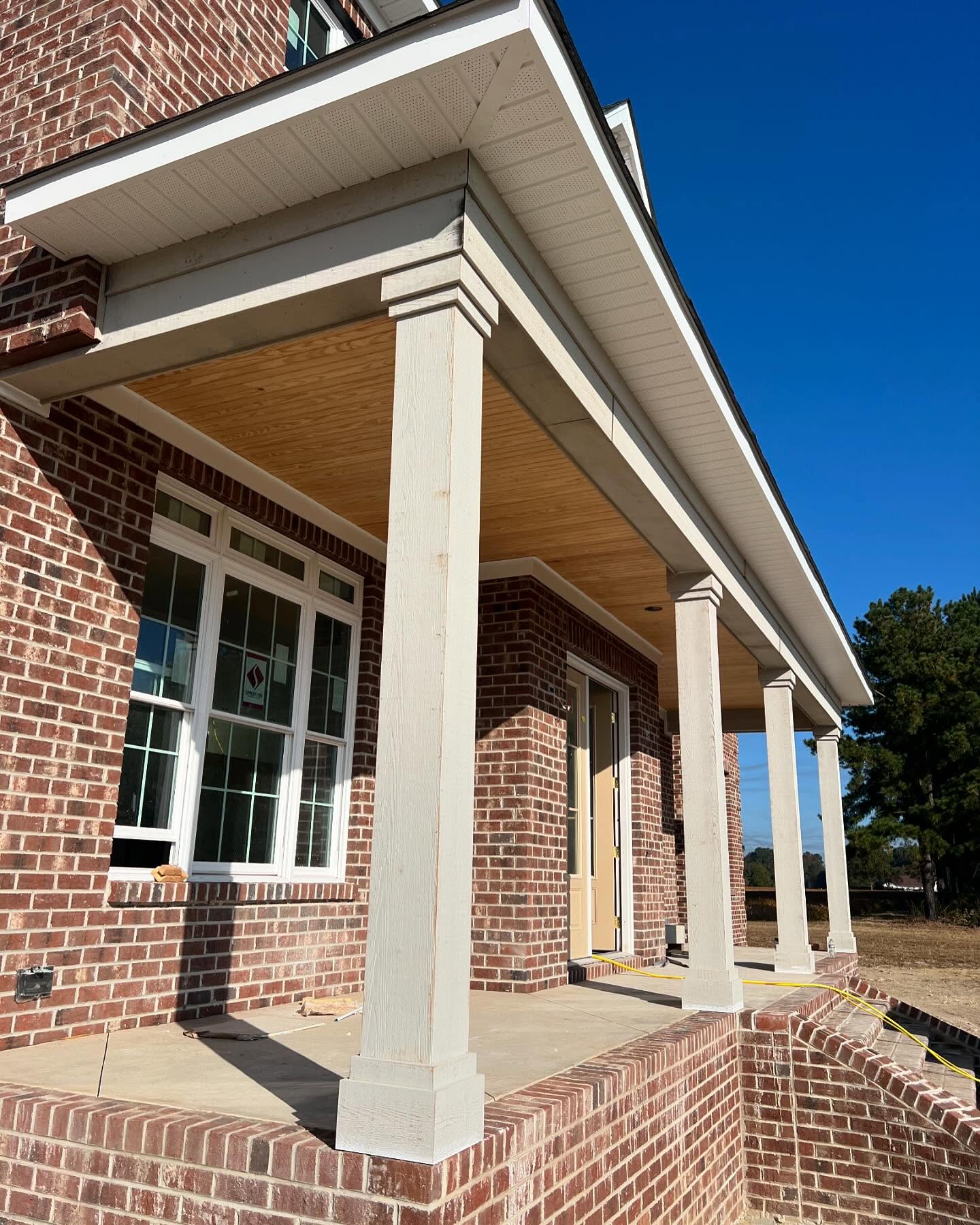 Covered brick porch with square painted columns, a tongue and groove wood ceiling and a poured concrete deck on a custom home