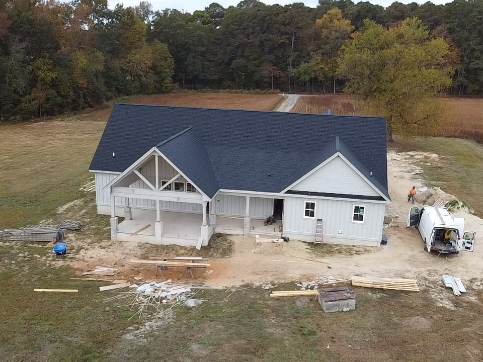Aerial view of a custom home showing a deep covered rear porch with exposed timber trusses under a gable