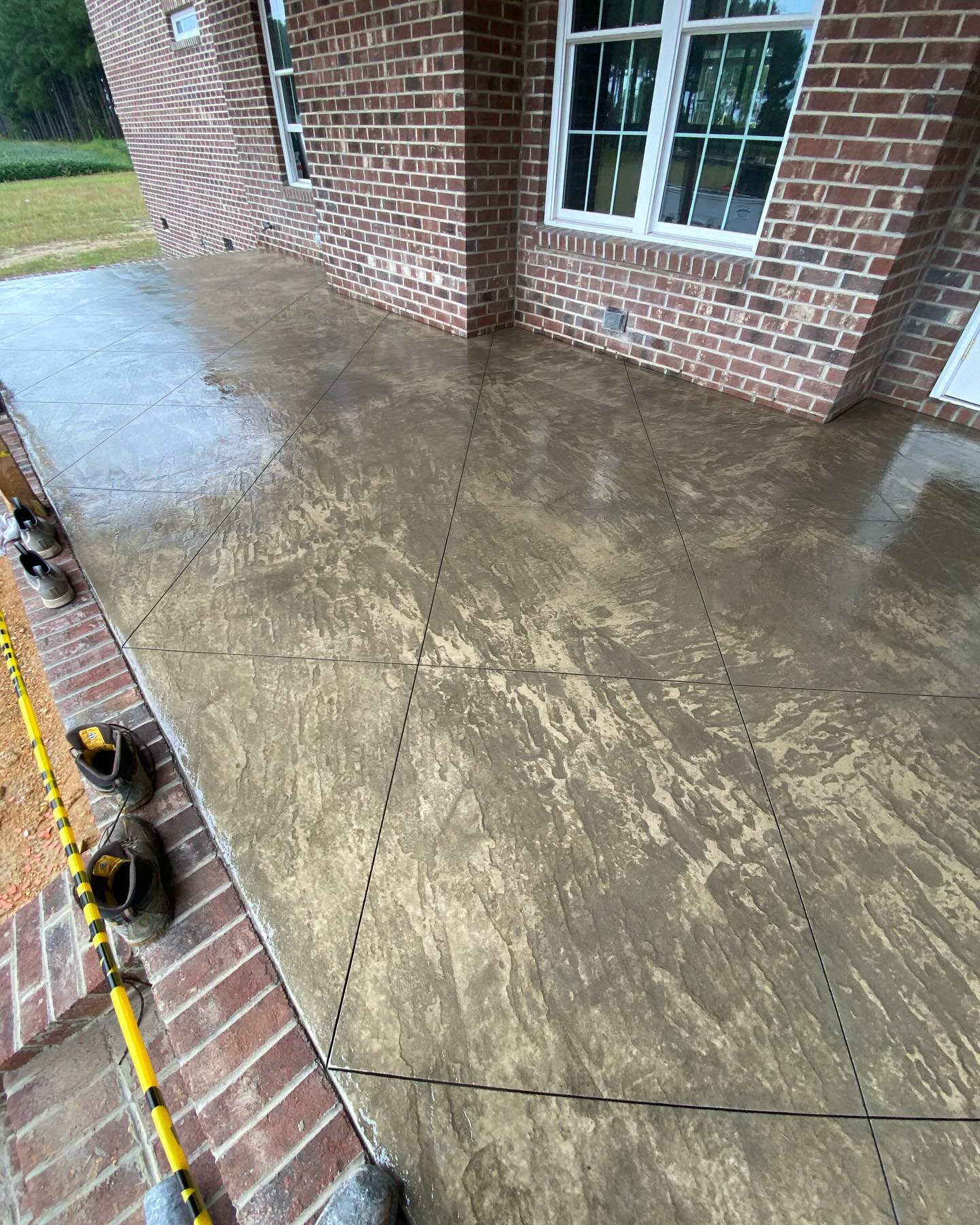 Large stamped and scored concrete patio running along the brick rear elevation of a custom home