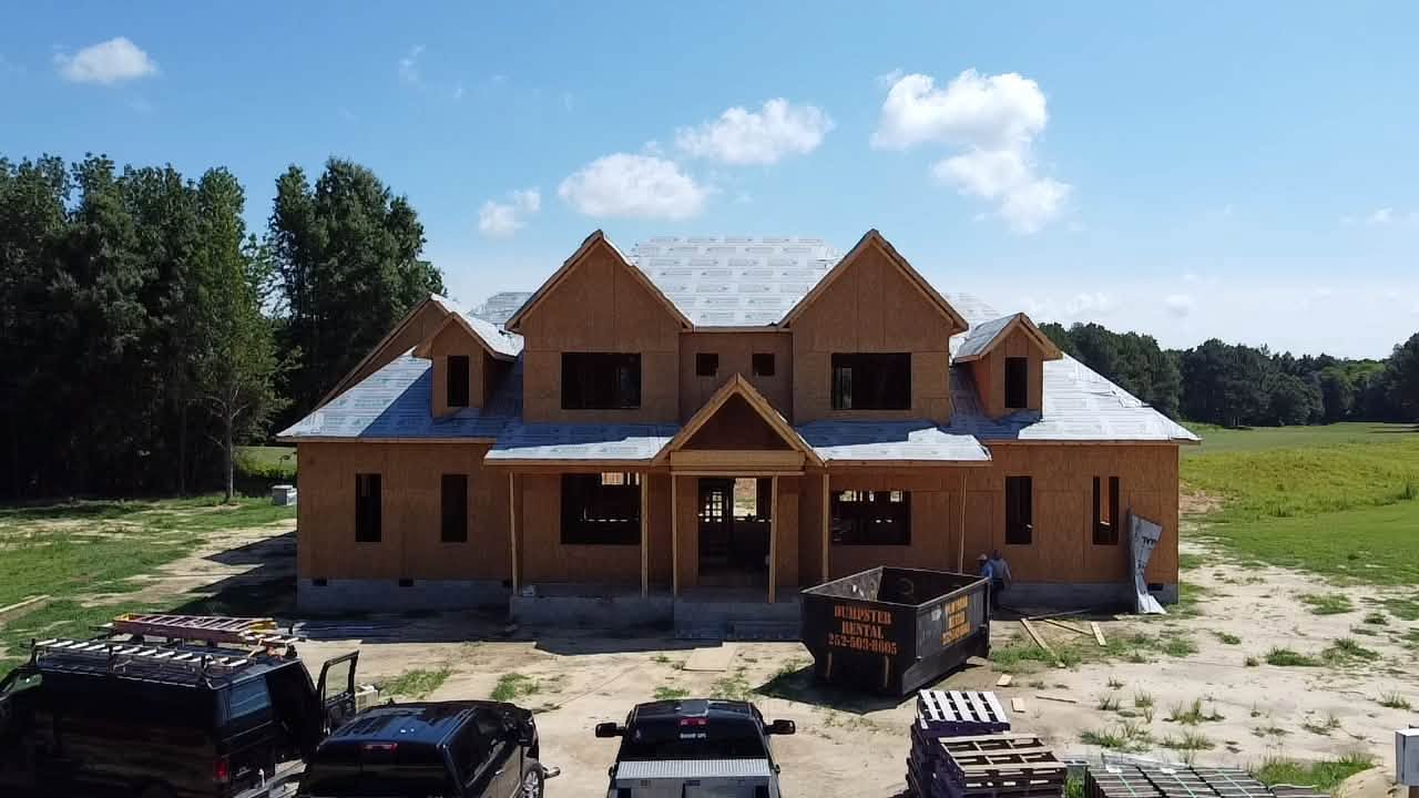 Front elevation of a two story custom home framed and dried in, with gabled dormers and a covered entry porch