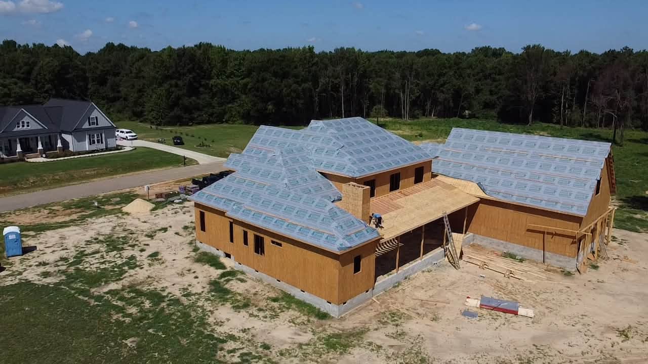 Aerial view of an L shaped custom home under construction with an attached garage wing
