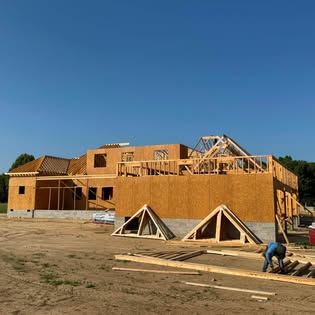 Ground level view of a custom home during wall and roof framing, with roof trusses staged on site