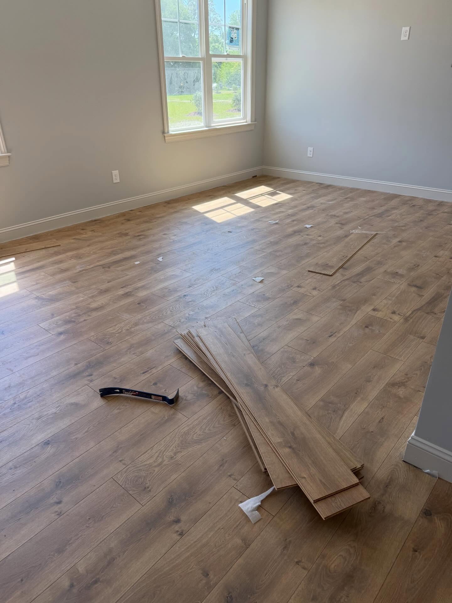 Interior room of a custom home during flooring installation, with planks laid across the floor and trim already in place