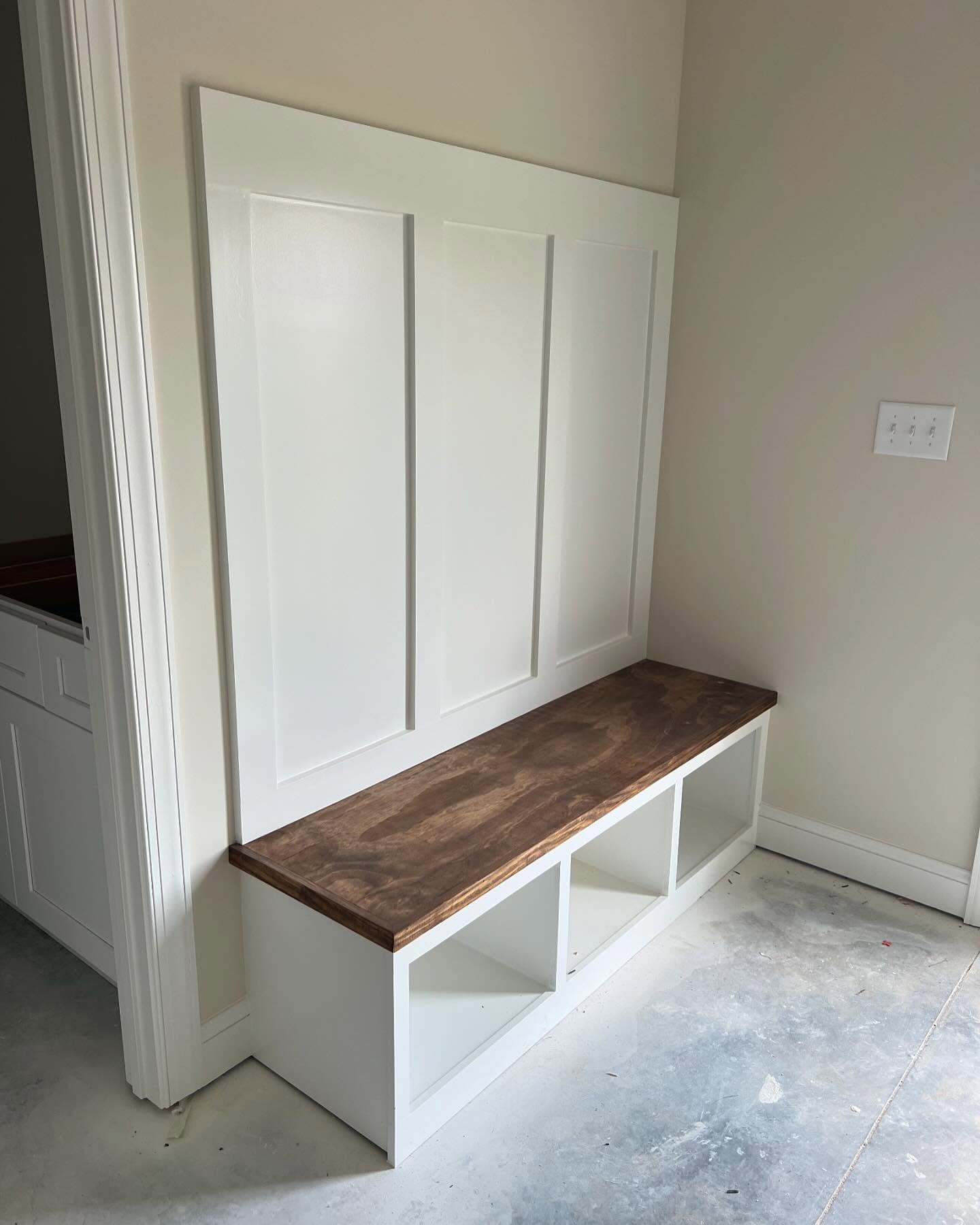 Custom mudroom bench with a stained wood top and white board and batten panelling above, built in place during interior trim