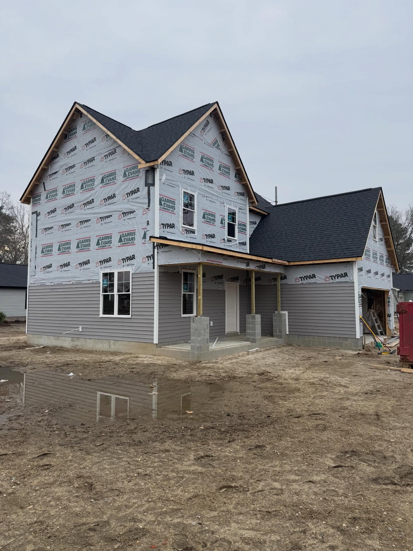 Two story custom home wrapped in housewrap with siding partly installed and the covered porch framed