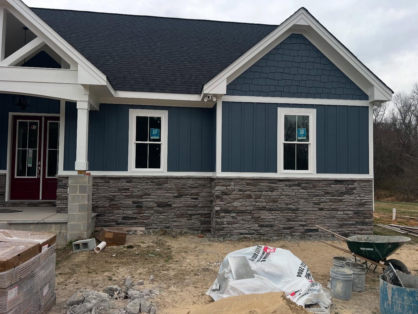 A Summerlin Contracting custom home mid build in Johnston County, with stone veneer going on over the foundation, mortar buckets and a wheelbarrow staged in front